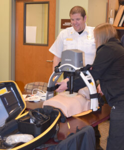 Manager Cliff Stoutenburg watches as EMT Shealyne Peasley secures the LUCAS device around the training manikin.